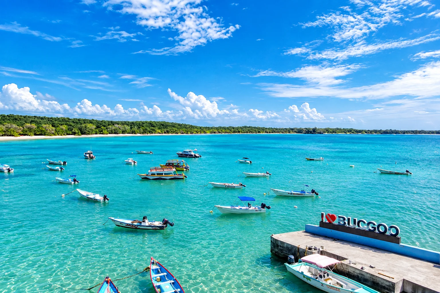 Turquoise Buccoo bay full of moored boats, with the I Love Buccoo sign on the jetty at right